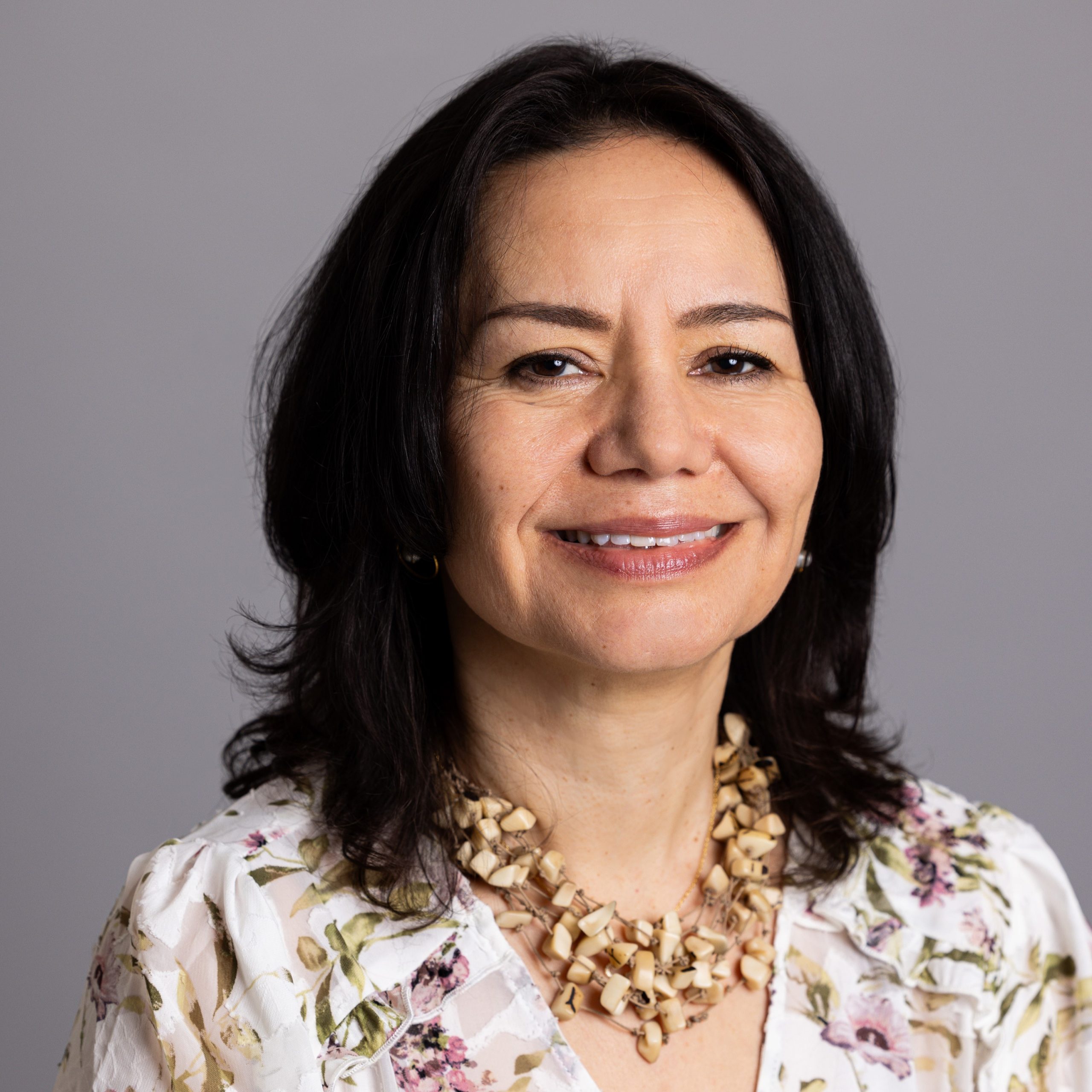 Mayte Restrepo smiling in photo with a gray background